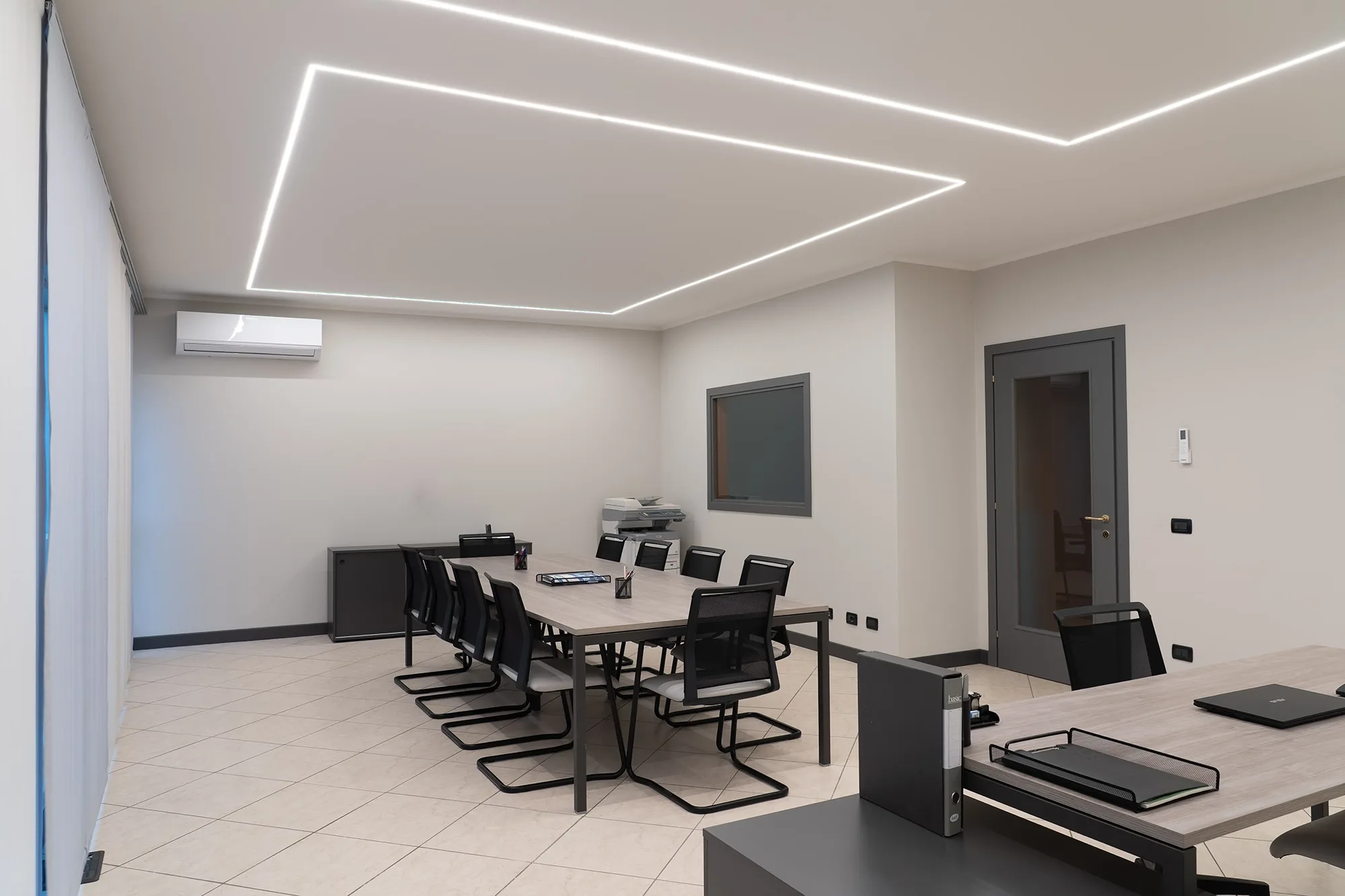 Sala riunioni moderna con tavolo lungo, sedie nere e illuminazione a LED